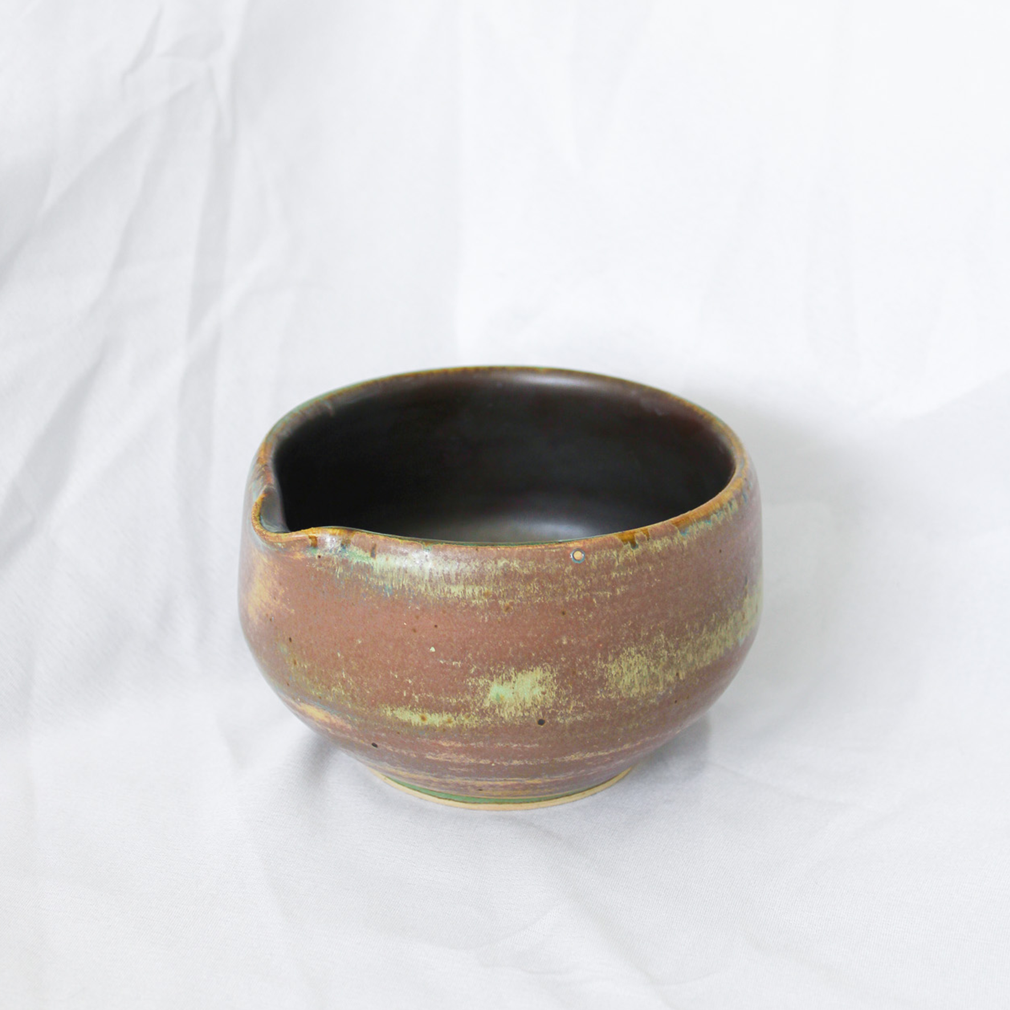 Ceramic bowl with brown and green glaze on a white background